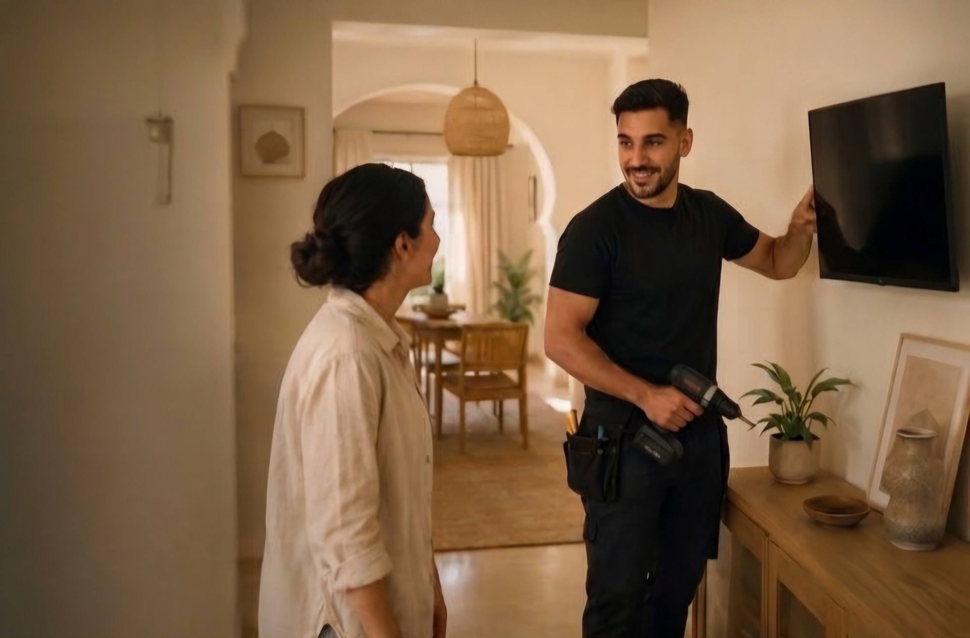 A trusted Sayebli helper mounting a TV in a warm home in Tangier while the homeowner looks on